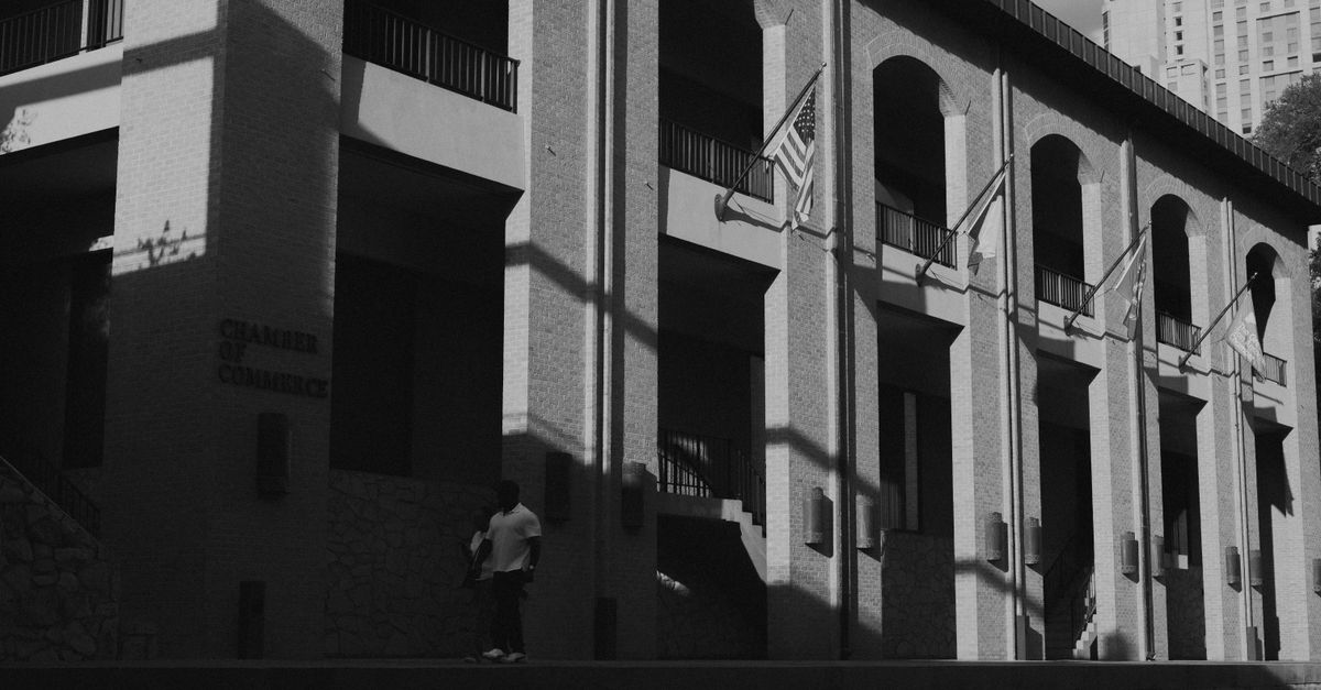 A black and white photo of the Chamber of Commerce building with dramatic shadows and flags.
